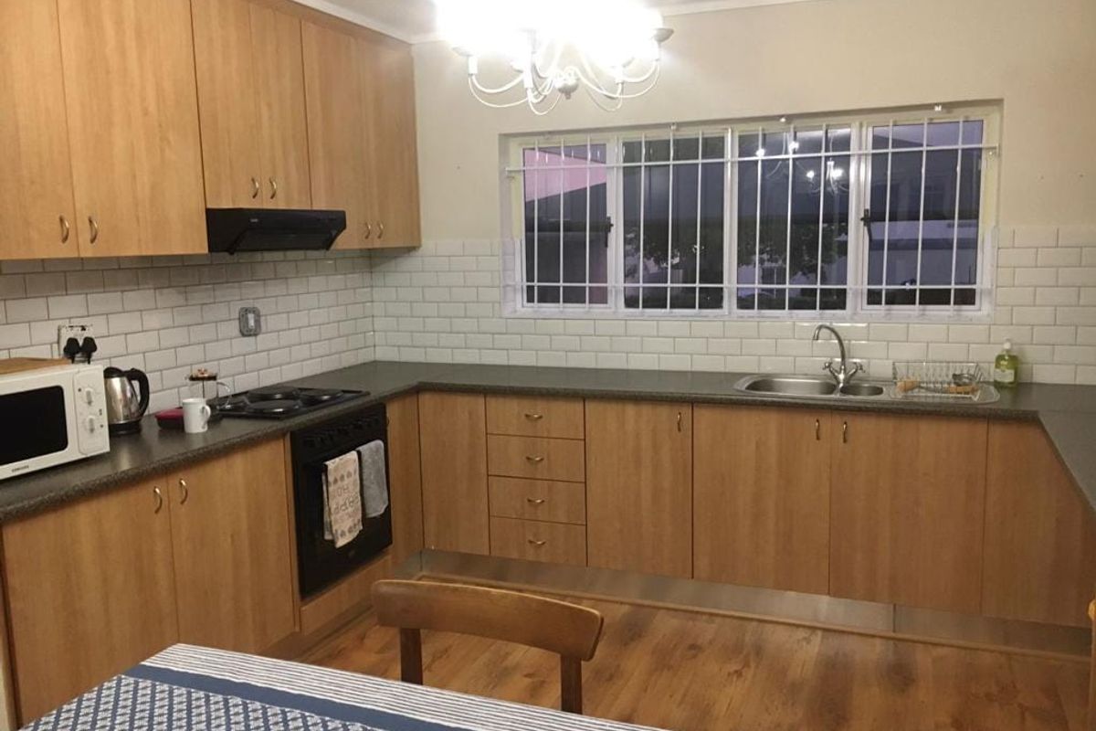 Functional kitchen featuring light wood cabinetry, subway tile backsplash, dark laminate countertops, and built-in cooking appliances with security bars on the window.