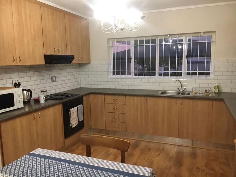 Functional kitchen featuring light wood cabinetry, subway tile backsplash, dark laminate countertops, and built-in cooking appliances with security bars on the window.