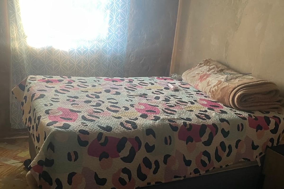 A bedroom featuring exposed plaster walls and a corrugated metal ceiling, requiring significant renovation to improve finishes and structural integrity.