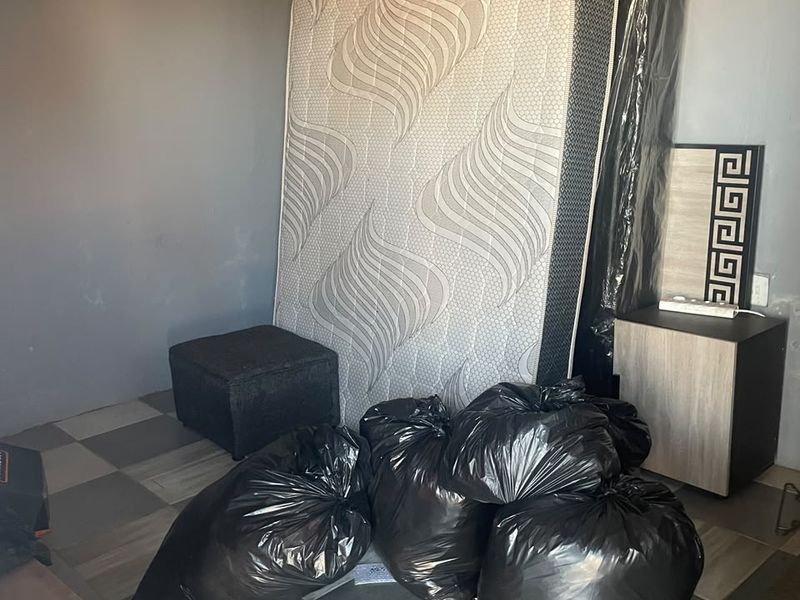 A bedroom space featuring tiled flooring and coved ceilings, currently used for storage with various items present.