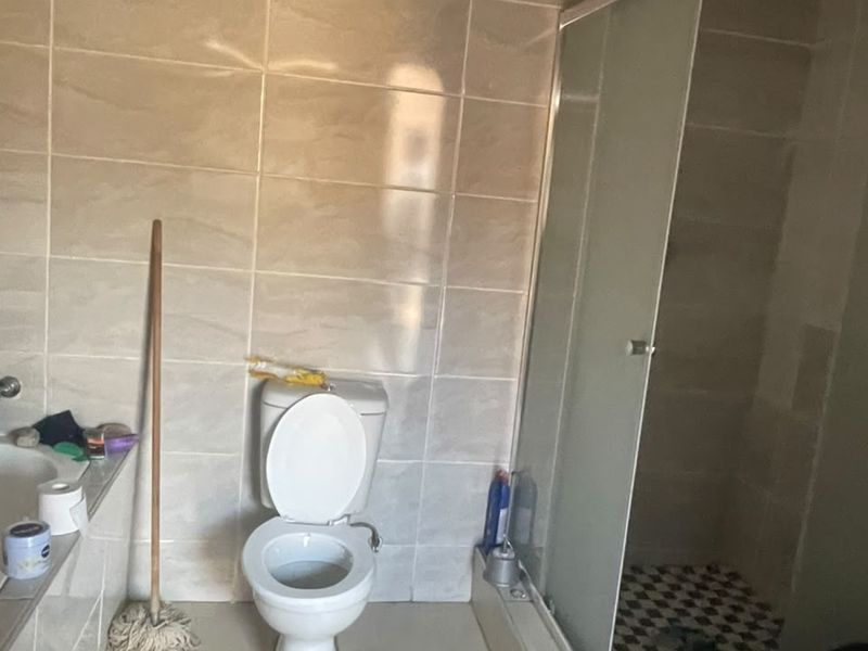 A functional bathroom featuring a shower enclosure, toilet, and vanity basin with tiled finishes, currently requiring ceiling completion.
