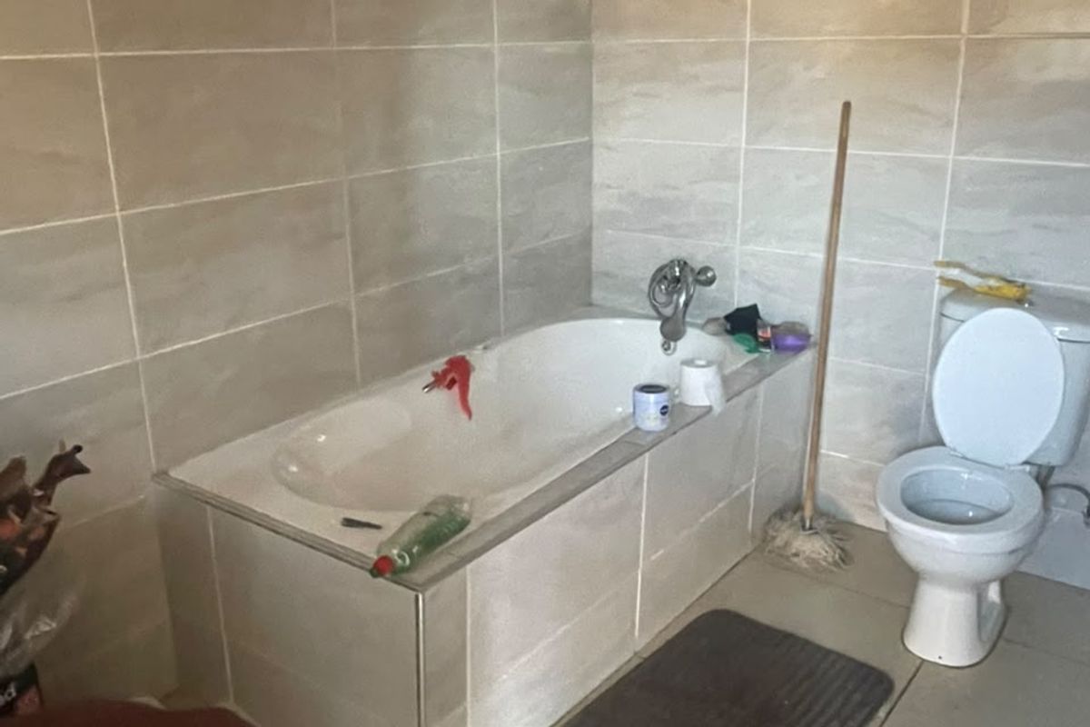 A functional bathroom featuring tiled walls and flooring, a built-in bathtub, and a standard toilet, currently requiring ceiling completion.
