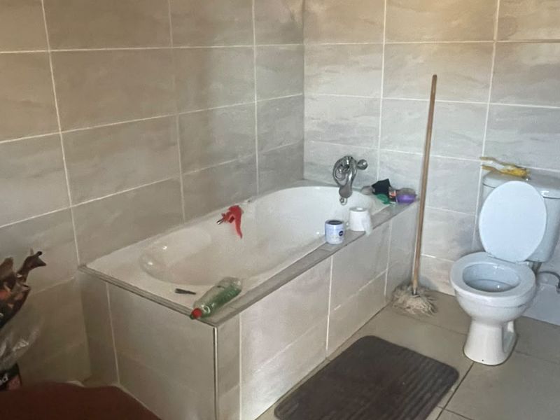 A functional bathroom featuring tiled walls and flooring, a built-in bathtub, and a standard toilet, currently requiring ceiling completion.