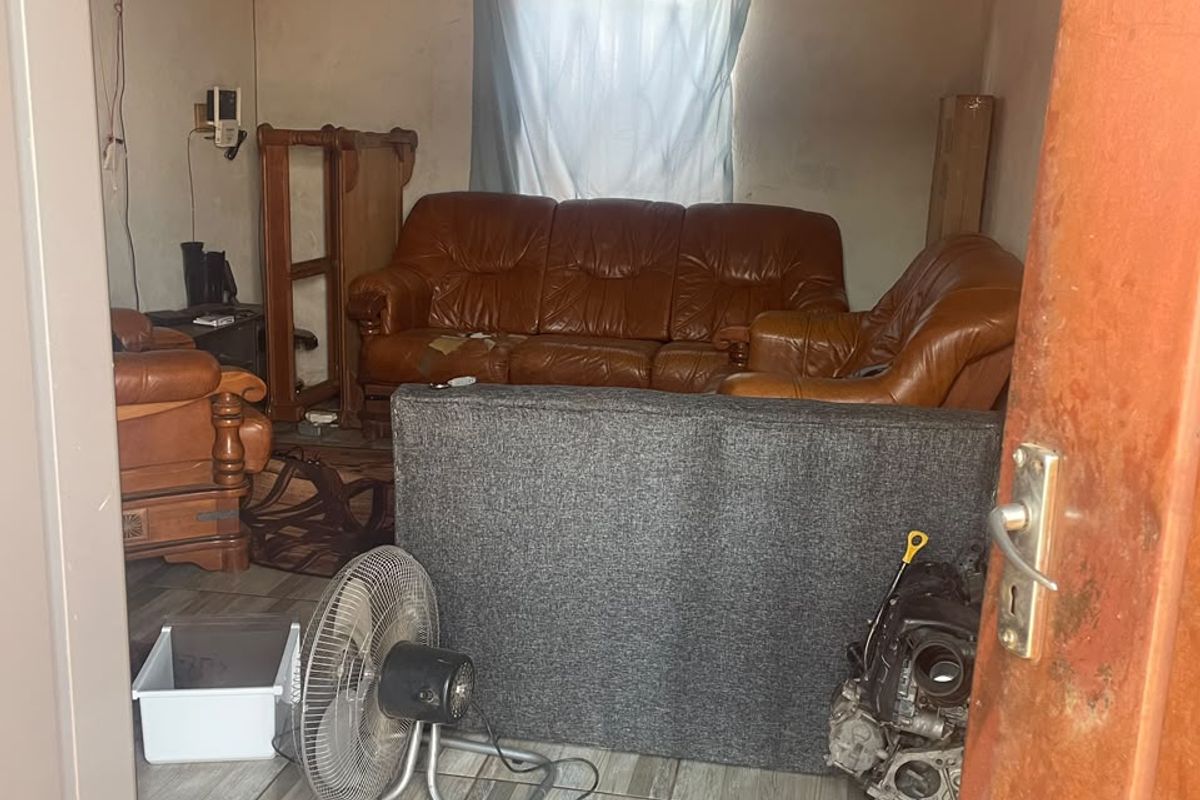 A small living area featuring tiled flooring and an exposed corrugated metal ceiling, currently in need of significant cosmetic renovation and wall repairs.