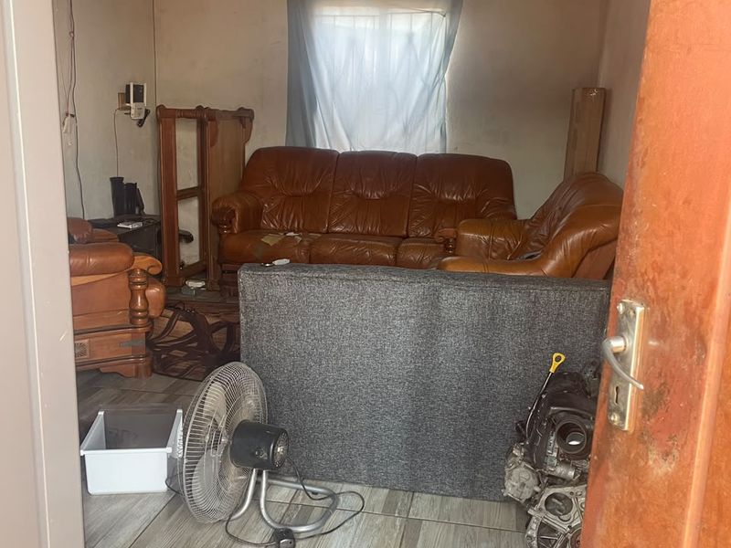 A small living area featuring tiled flooring and an exposed corrugated metal ceiling, currently in need of significant cosmetic renovation and wall repairs.