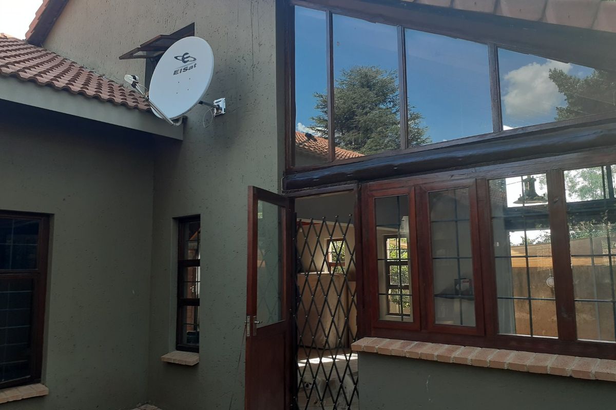 Rear exterior view of the property featuring a satellite dish, timber-framed windows, and a security gate entrance.