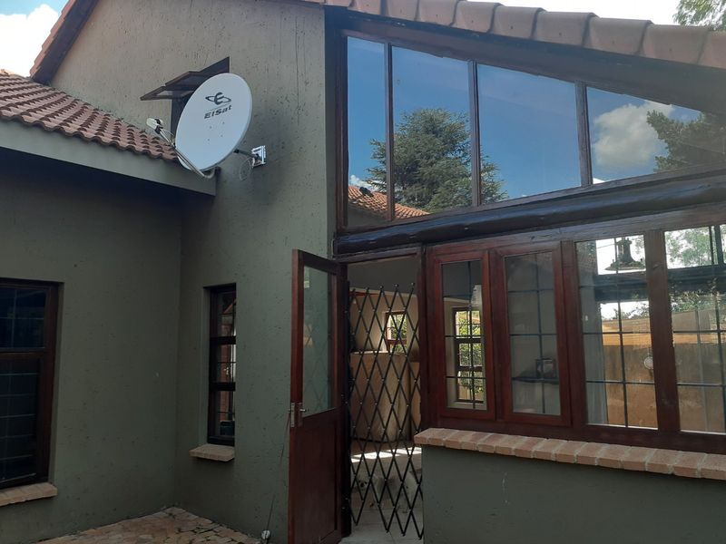 Rear exterior view of the property featuring a satellite dish, timber-framed windows, and a security gate entrance.