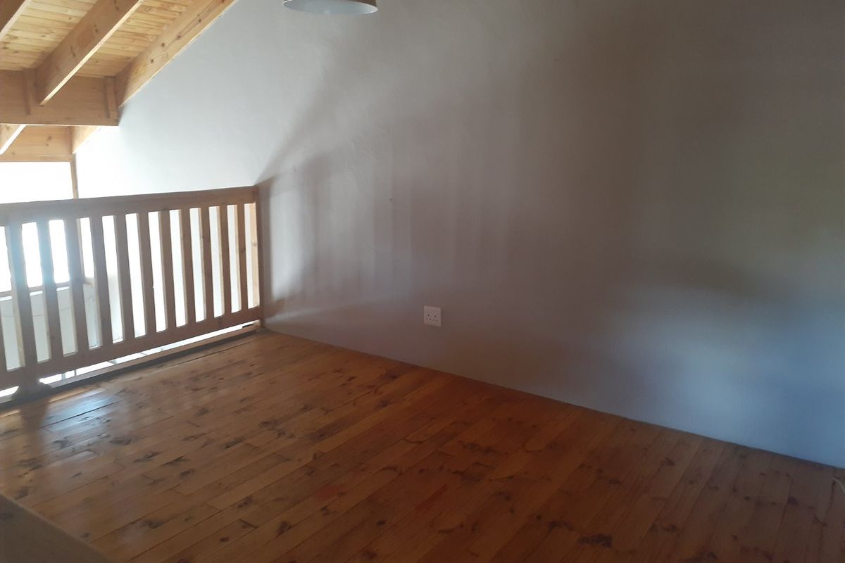 An empty loft-style bedroom featuring exposed timber ceiling beams, polished timber flooring, and a wooden balustrade overlooking the lower level.