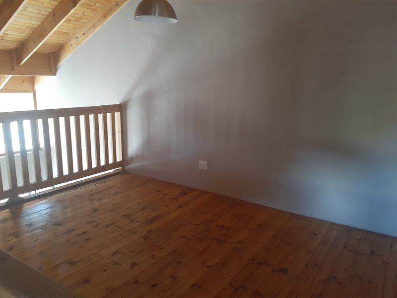 An empty loft-style bedroom featuring exposed timber ceiling beams, polished timber flooring, and a wooden balustrade overlooking the lower level.