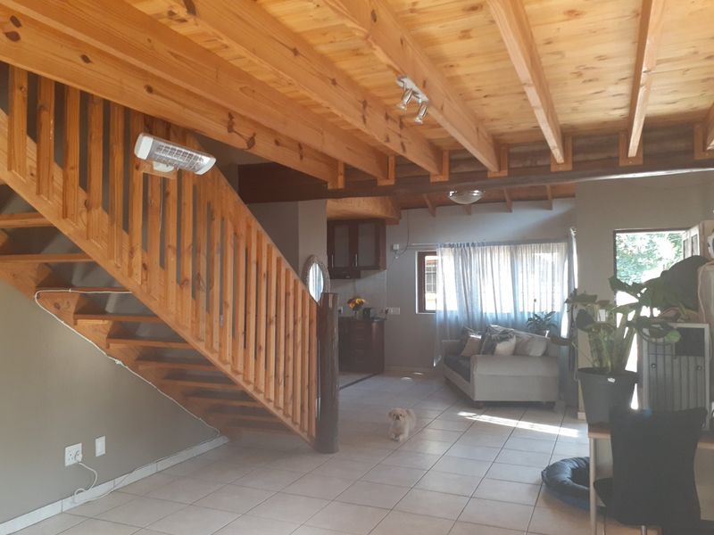 Open-plan living area featuring exposed timber beam ceilings, tiled flooring, and a wooden staircase leading to the upper level.