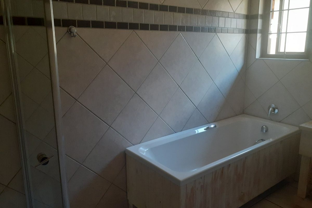 A functional bathroom featuring a built-in bathtub, shower enclosure, and neutral wall tiling with a decorative border.