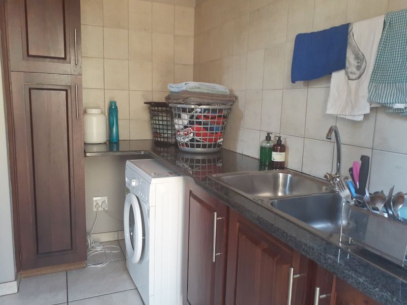 Functional laundry area featuring dark wood cabinetry, granite countertops, a double stainless steel sink, and tiled wall finishes.