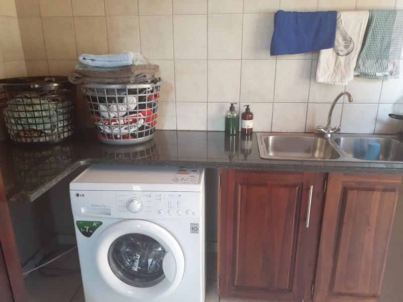 A functional laundry area featuring a granite countertop, stainless steel double sink, and wooden cabinetry with a tiled backsplash.