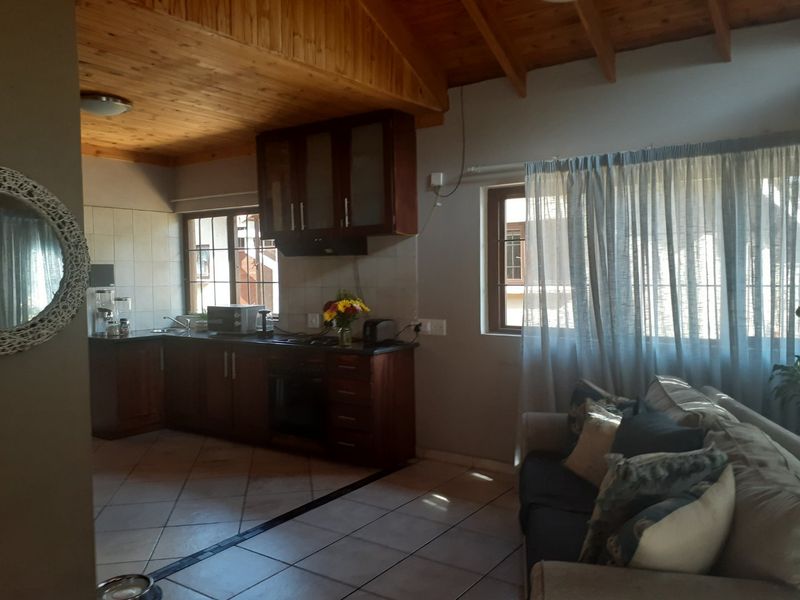 Open-plan kitchen and living area featuring a timber vaulted ceiling, tiled flooring, and dark wood cabinetry with integrated appliances.