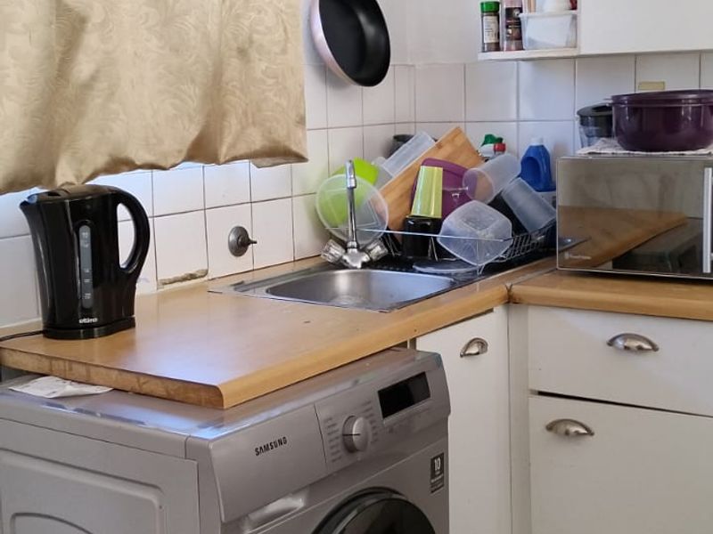 A compact kitchen area featuring built-in cabinetry, a stainless steel sink, tiled splashback, and tiled flooring, providing functional utility space.