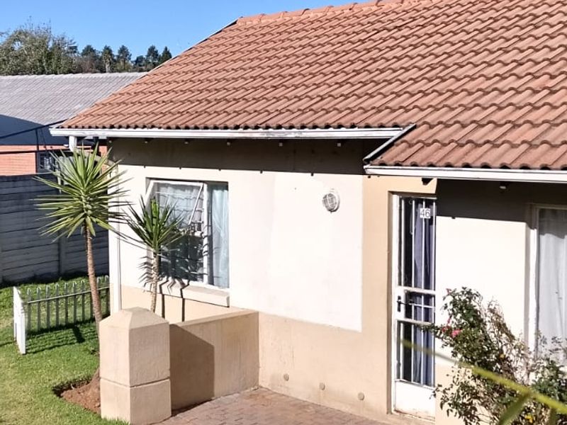 Front exterior view of the apartment featuring a tiled roof, a small brick-paved patio area, and a metal perimeter fence.