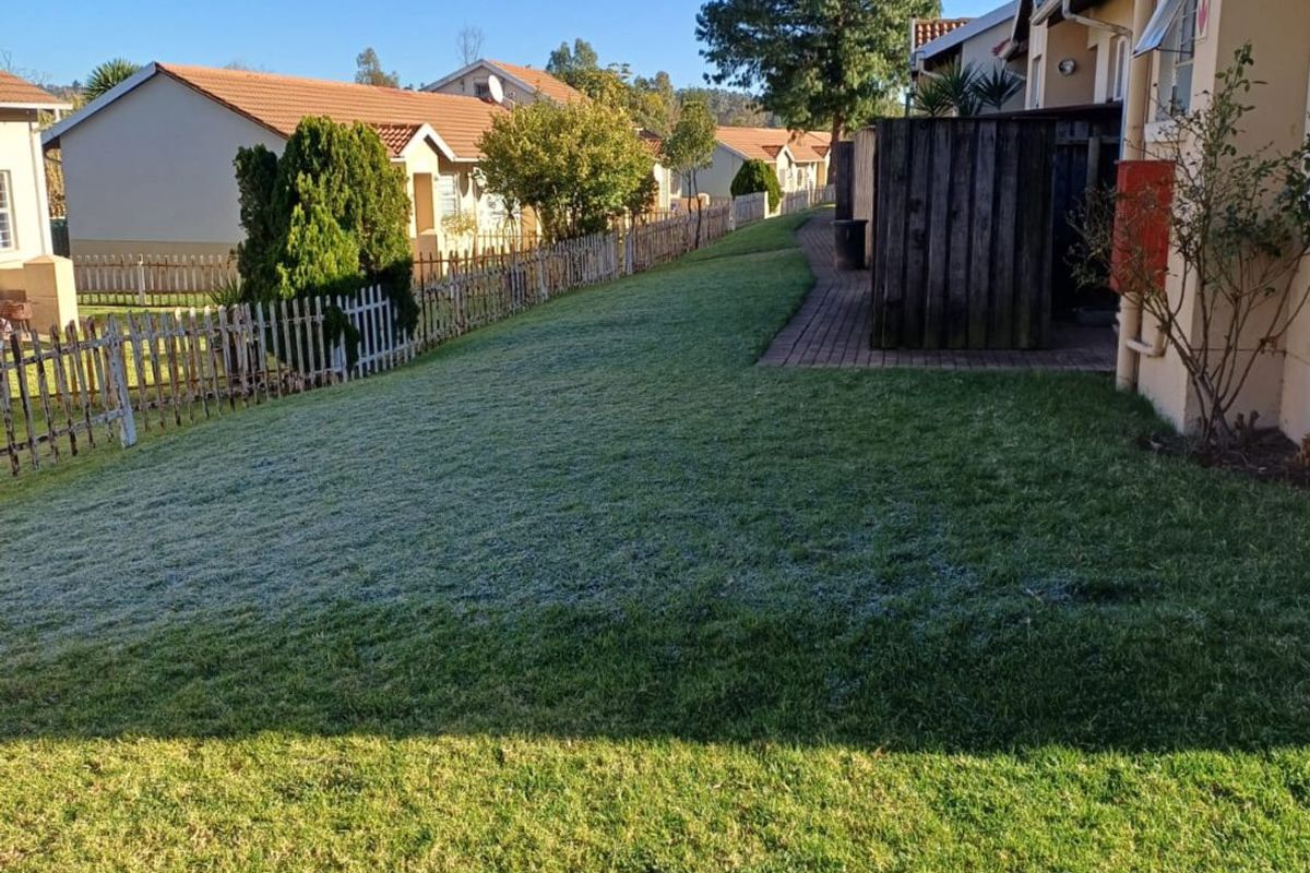 A rear garden area featuring a lawn, paved walkway, and wooden privacy screen, enclosed by a picket fence.