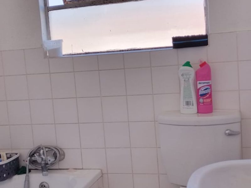 A functional bathroom featuring a bathtub, pedestal basin, and toilet with white wall tiles and tiled flooring, requiring cosmetic updates.