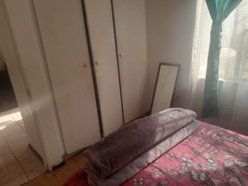A bedroom featuring built-in cupboards and laminate flooring, with natural light entering through the window.