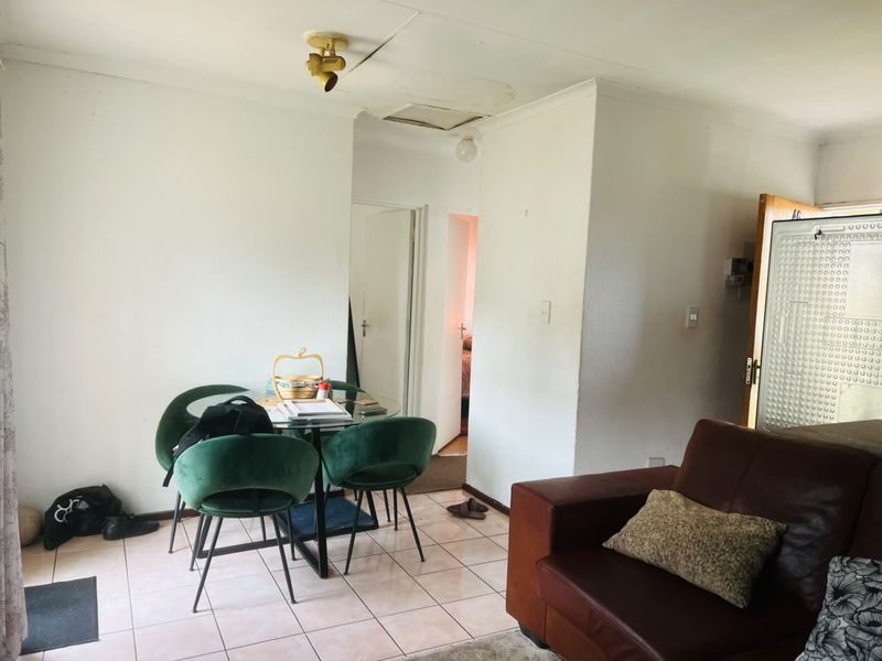 Open plan living and dining area featuring tiled flooring and visible ceiling damage requiring maintenance.
