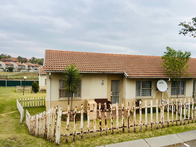 Front view of a single-story apartment unit featuring a tiled roof, security gate, and a private garden area enclosed by a picket fence.