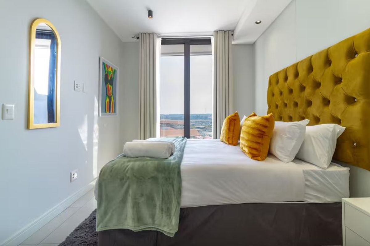 A well-maintained bedroom featuring modern recessed lighting, neutral finishes, and a large window providing natural light and an elevated view.
