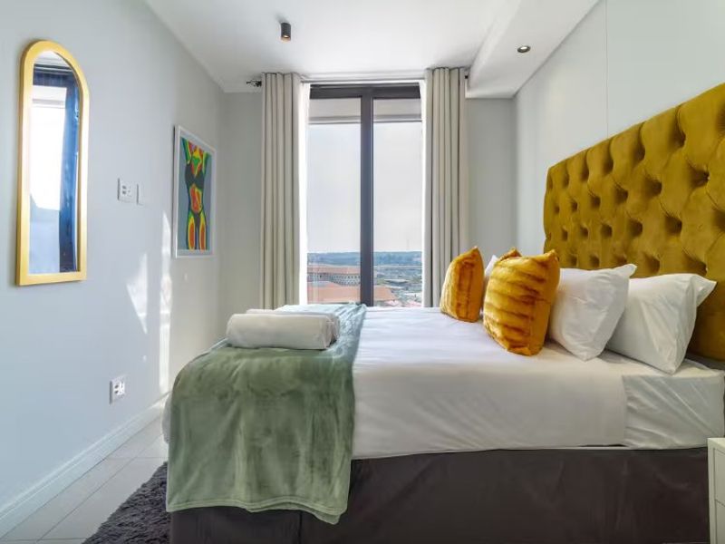 A well-maintained bedroom featuring modern recessed lighting, neutral finishes, and a large window providing natural light and an elevated view.