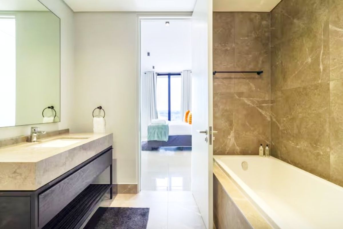 Modern bathroom featuring a floating vanity with stone countertop, undermount sink, and a built-in bathtub with elegant marble-look wall tiling.