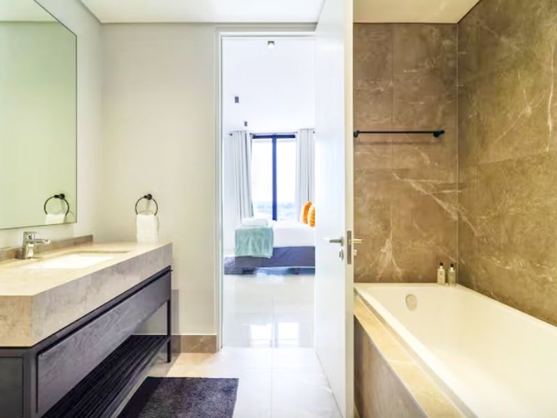 Modern bathroom featuring a floating vanity with stone countertop, undermount sink, and a built-in bathtub with elegant marble-look wall tiling.