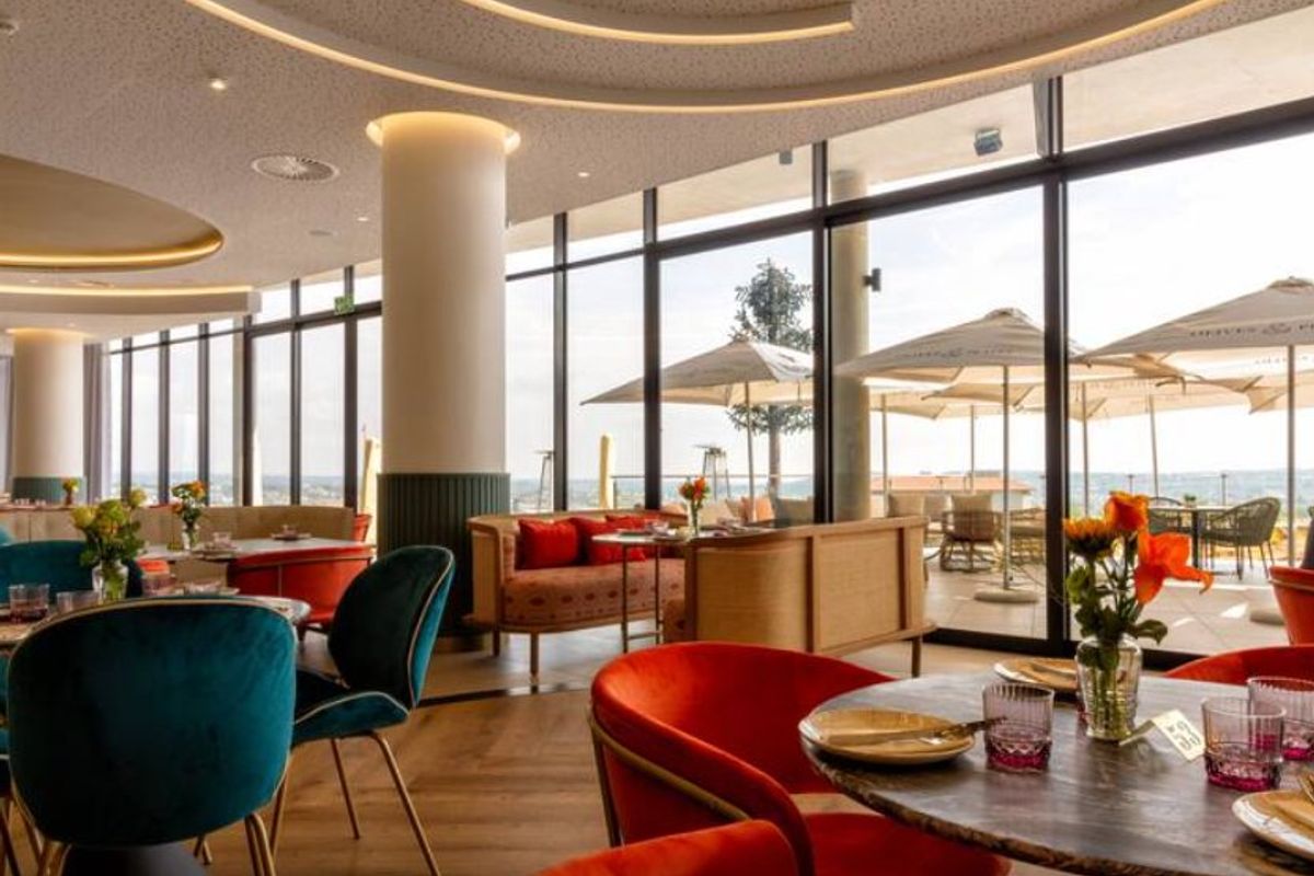 A modern, high-end open-plan dining area featuring floor-to-ceiling windows, recessed ceiling lighting, and expansive views of an outdoor terrace.