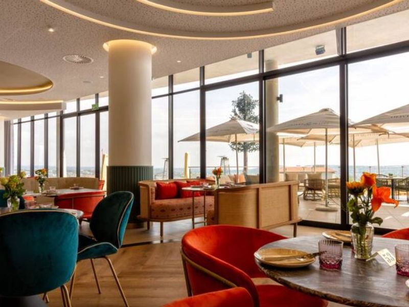 A modern, high-end open-plan dining area featuring floor-to-ceiling windows, recessed ceiling lighting, and expansive views of an outdoor terrace.