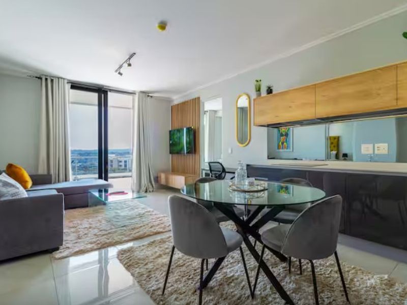 Modern open-plan living and dining area featuring sleek cabinetry, a mirrored splashback, and large sliding doors leading to a balcony with scenic views.