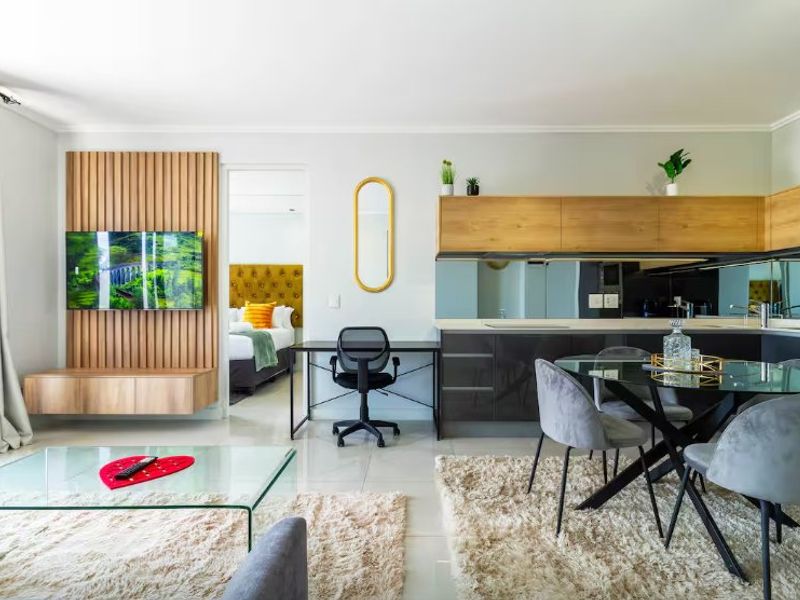 Modern open-plan living area featuring a timber slat feature wall, sleek kitchen cabinetry with mirrored splashback, and seamless tiled flooring throughout.