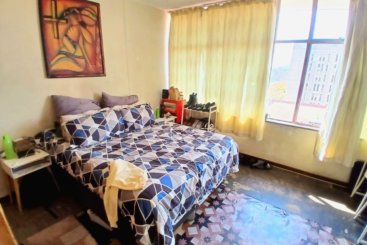 A bedroom featuring a large window with natural light and patterned floor tiles, currently showing signs of wear and requiring cosmetic updates.