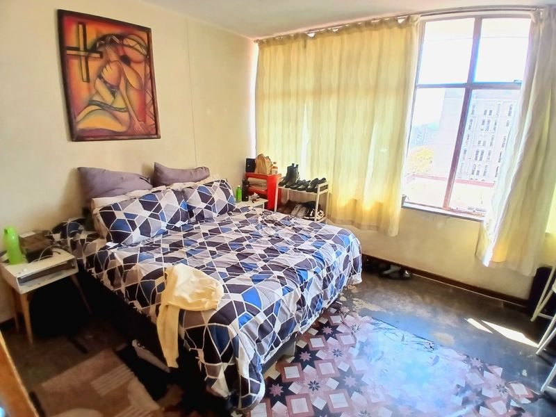 A bedroom featuring a large window with natural light and patterned floor tiles, currently showing signs of wear and requiring cosmetic updates.