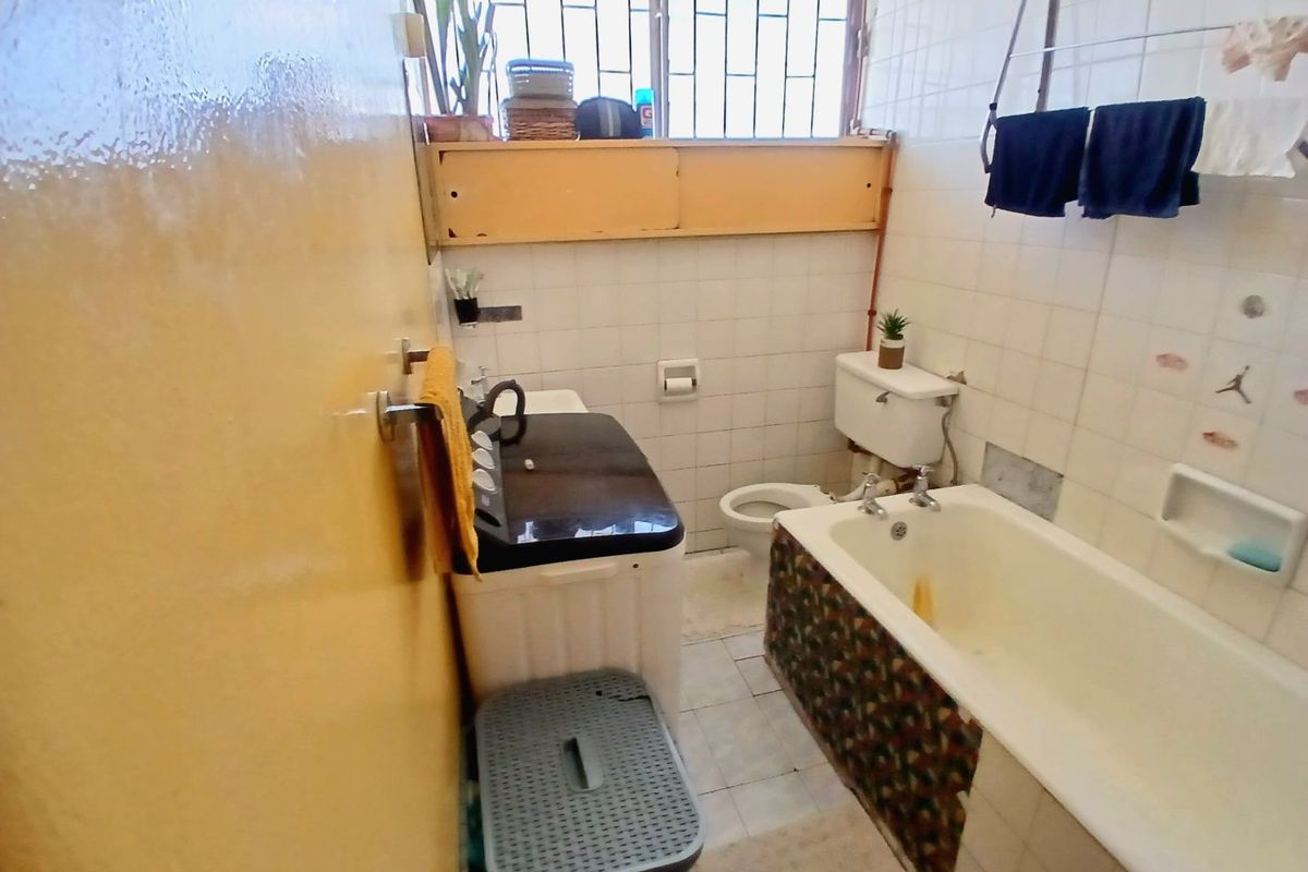 A compact bathroom featuring a bathtub, toilet, and tiled finishes. The space is dated and would benefit from a modern renovation.