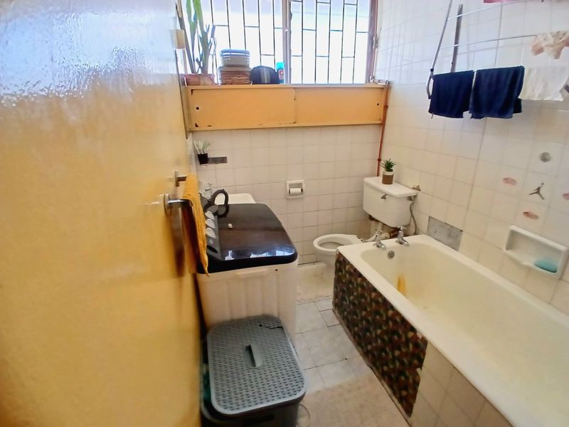 A compact bathroom featuring a bathtub, toilet, and tiled finishes. The space is dated and would benefit from a modern renovation.