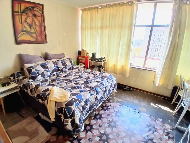 A bedroom featuring a large window providing natural light and tiled flooring in need of maintenance or replacement.