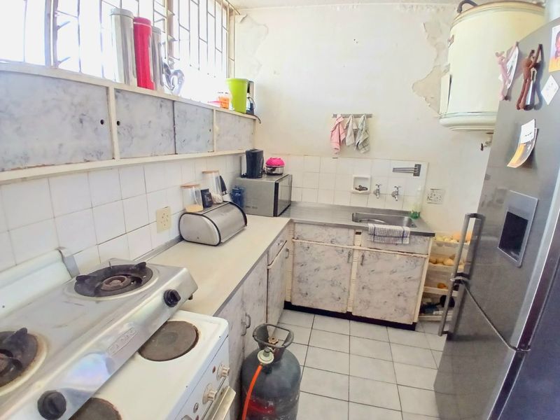 A dated kitchen featuring tiled flooring, built-in cabinetry, and a stainless steel sink, requiring significant cosmetic updates and wall repairs.