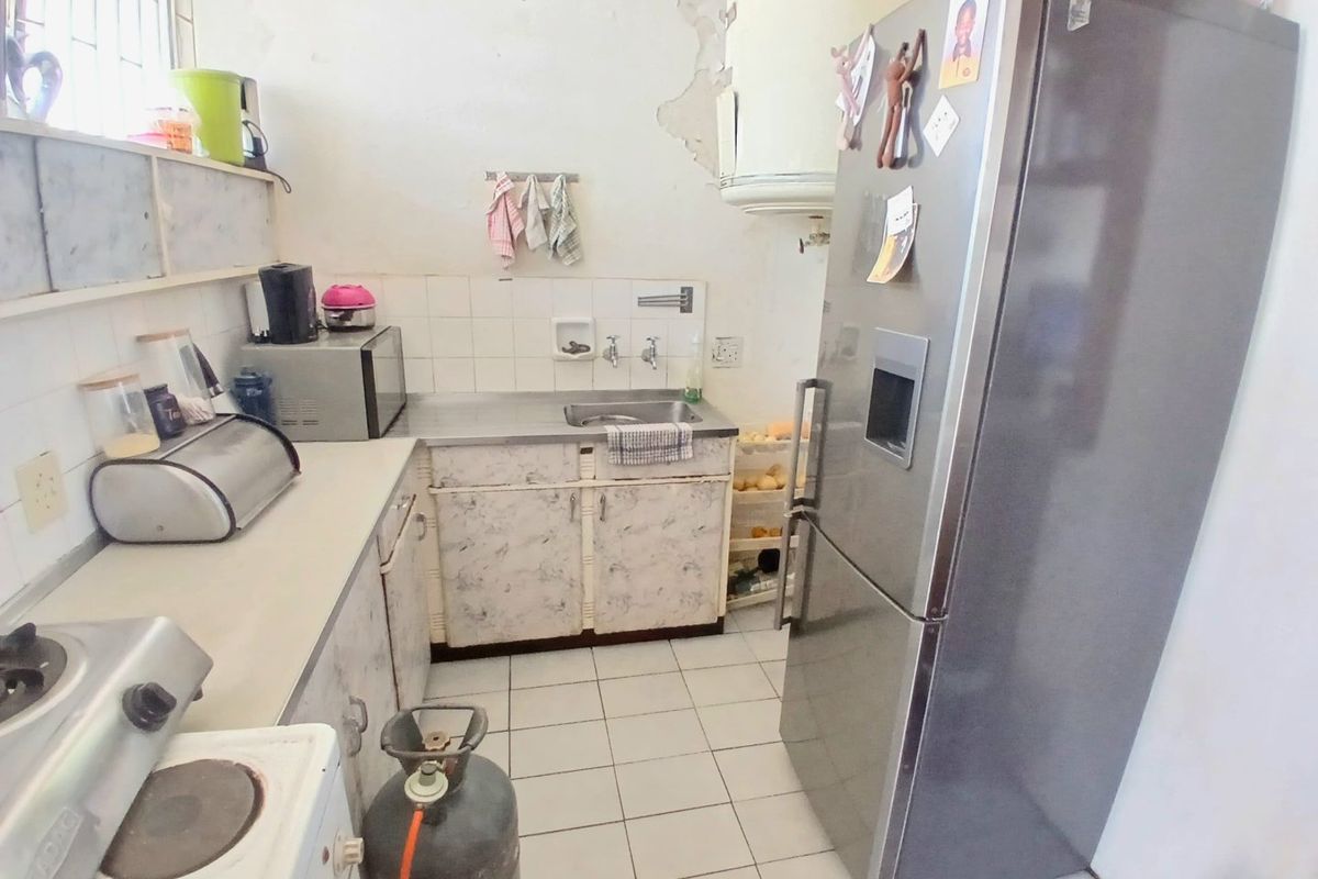 A compact kitchen featuring tiled flooring, a stainless steel sink, and built-in cabinetry, currently showing significant wear and requiring cosmetic updates.