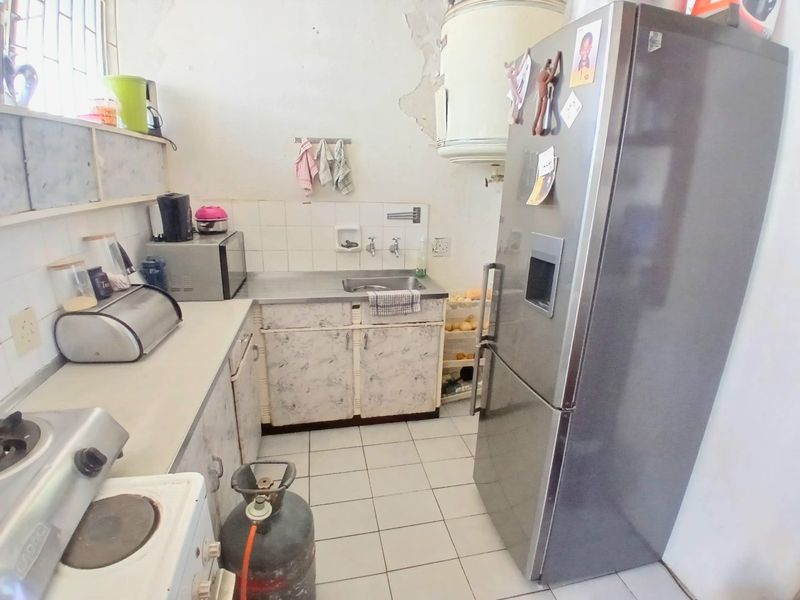 A compact kitchen featuring tiled flooring, a stainless steel sink, and built-in cabinetry, currently showing significant wear and requiring cosmetic updates.