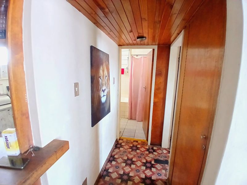 A narrow hallway featuring timber ceiling paneling and patterned floor tiles, leading towards a bathroom area.