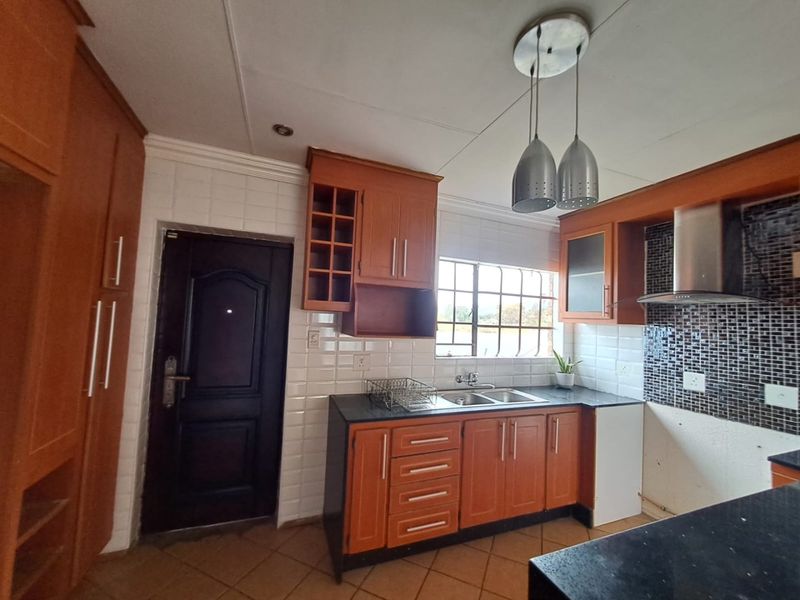 A functional kitchen featuring wooden cabinetry, a double basin sink, tiled backsplash, and an extractor fan, offering a practical layout for culinary activities.