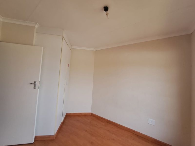A clean, empty bedroom featuring laminate flooring, neutral walls, and built-in cupboards, ready for personalization.