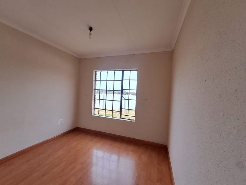 A vacant bedroom featuring laminate flooring, neutral walls, and a window fitted with security bars.