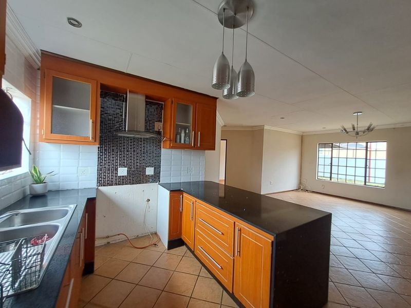 Open plan kitchen and living area featuring wooden cabinetry, granite countertops, and tiled flooring. The kitchen space requires a stove and minor wall repairs.