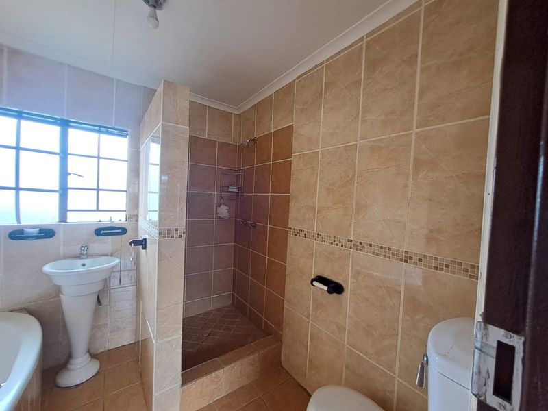 A functional bathroom featuring a pedestal basin, a walk-in shower with tiled finishes, and a standard toilet.