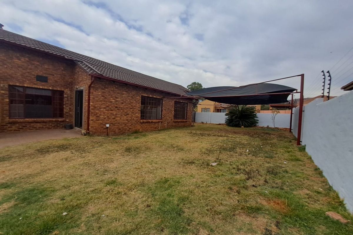 Rear view of a face brick house featuring a concrete patio, a shade cloth carport, and a perimeter wall with electric fencing.