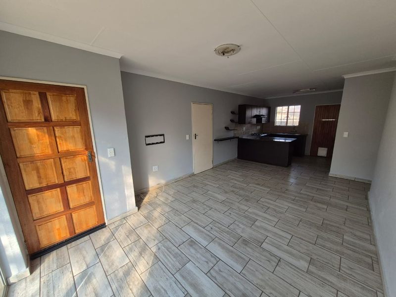 An open-plan living and kitchen area featuring tiled flooring, dark kitchen cabinetry with an island, and a solid wood front entrance door.
