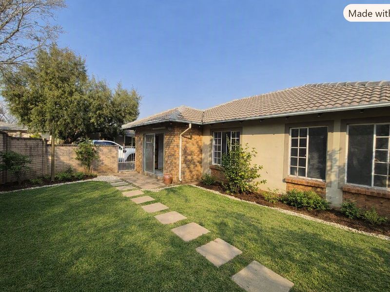 A well-maintained rear exterior view of a townhouse featuring a brick facade, tiled roof, and a landscaped garden with a concrete paver path.